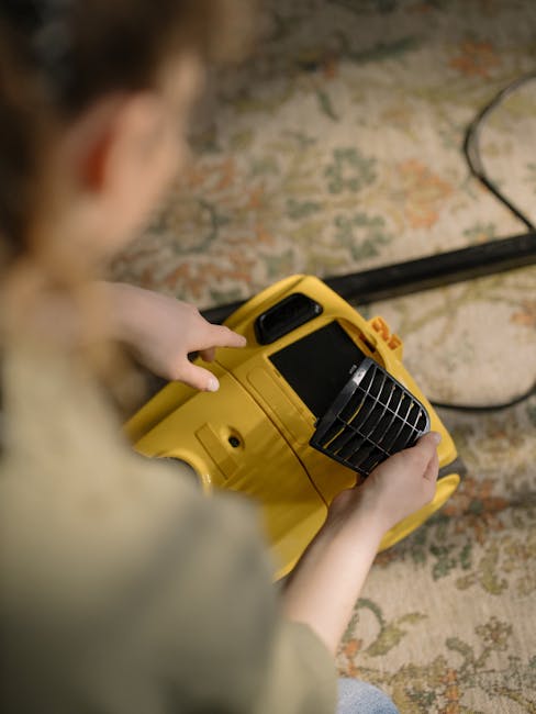 A person operating a yellow portable air mover or fan on a patterned area rug in a room with exposed brick wall, likely engaged in surface cleaning or deodorising processes to help eliminate pet odour